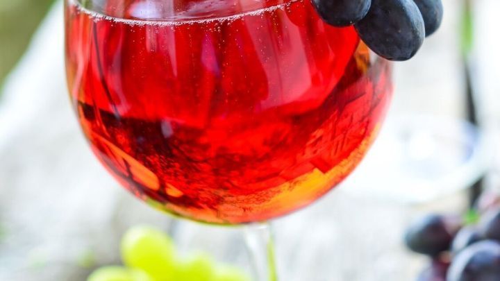 Ein Weinglas mit roten Trauben steht auf einem rustikalen Holzuntergrund, umgeben von gr&uuml;nen und roten Trauben.