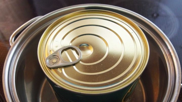Ein gl&auml;nzender, goldfarbener Konservendosedeckel liegt auf einem Topf, w&auml;hrend das Wasser darin kocht.
