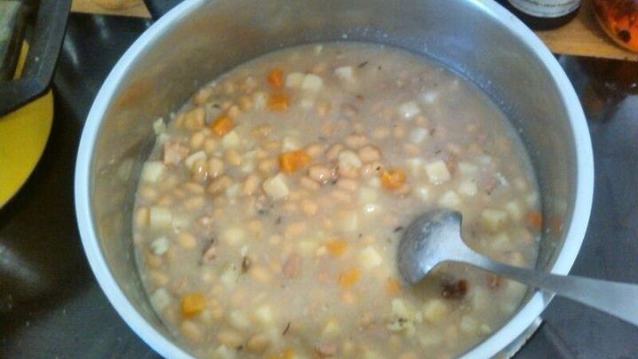 Eine gro&szlig;e Kochtopf mit Bohnensuppe auf italienische Art k&ouml;chelt, umgeben von K&uuml;chenger&auml;ten und Gew&uuml;rzen.