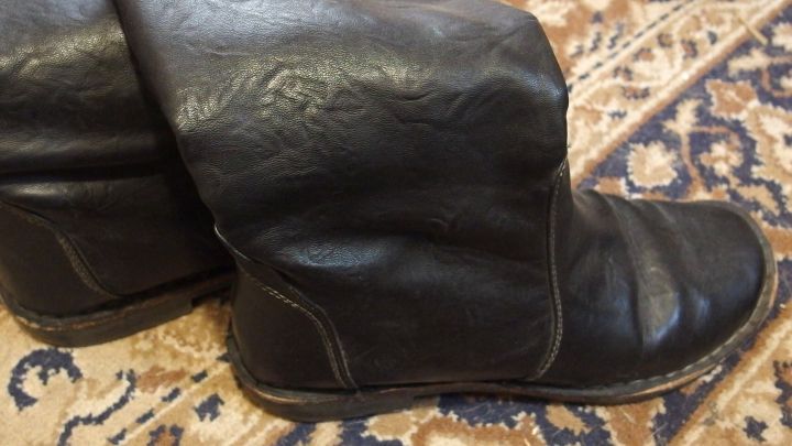 Schwarze Glattleder-Stiefel stehen auf einem Teppich und wirken eng, bereit zum Dehnen mit hei&szlig;em Wasser.