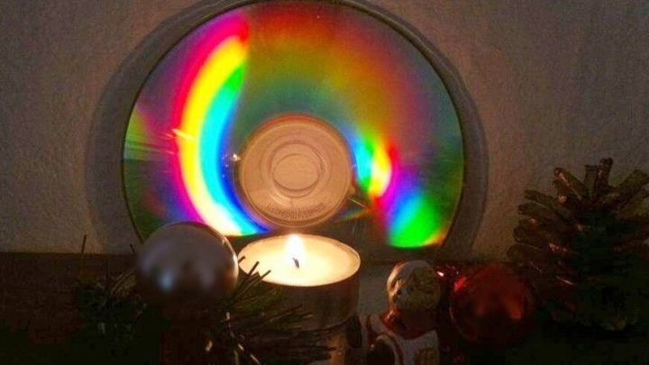 Ein altes CD reflektiert buntes Licht, w&auml;hrend ein Teelicht in der Mitte flackert, umgeben von Weihnachtsdekoration.