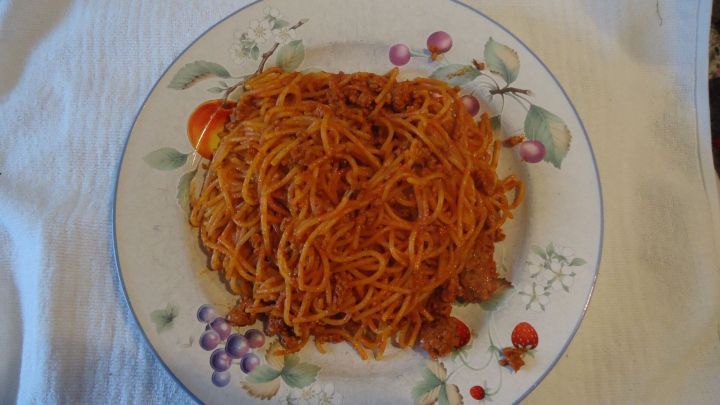 Auf einem Teller liegen Tomatenspaghetti, die appetitlich angerichtet sind, auf einem wei&szlig;en Untergrund.