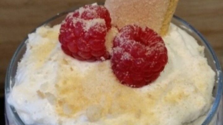 Ein Glas gef&uuml;llt mit cremigem Dessert, das frische Himbeeren und einen Keks auf der Oberfl&auml;che hat.