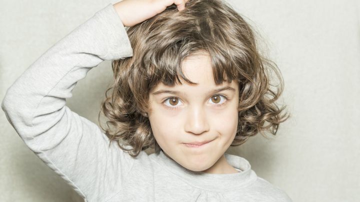 Ein Kind kratzt sich am Kopf und sieht neugierig aus, was auf m&ouml;gliche Parasiten beim Menschen hindeutet.