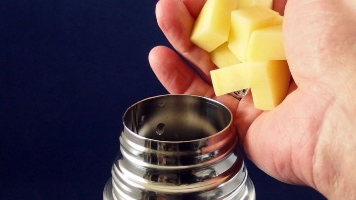 Eine Hand gibt gew&uuml;rfelte Kartoffeln in eine offene Thermoskanne, um sie zur Reinigung zu verwenden.