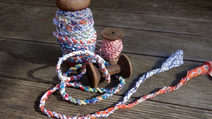 Bunte Geschenkband und Kordeln aus Stoffresten liegen auf einem rustikalen Holztisch, einige aufgewickelt, andere lose.