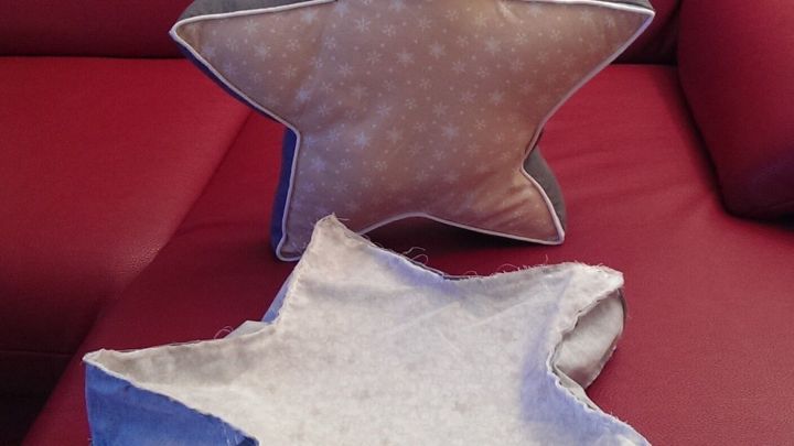 Ein Kissen in Sternenform liegt auf einer roten Couch, w&auml;hrend ein weiteres Kissen auf die Seite gewendet ist.