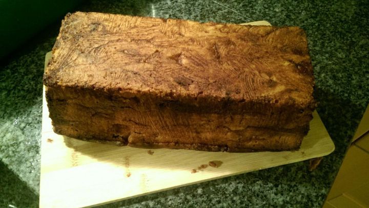 Ein Zimtkuchen mit Apfelst&uuml;cken liegt auf einem Holzbrett, umgeben von einer dunklen, strukturierten Arbeitsfl&auml;che.