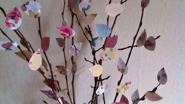 Zweige mit bunten Papierbl&auml;ttern zieren eine Vase, dekorativ arrangiert in einem hellen Raum.