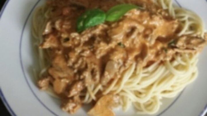 Ein Teller Spaghetti mit Bolognese So&szlig;e wird appetitlich serviert, garniert mit einem frischen Basilikumblatt.