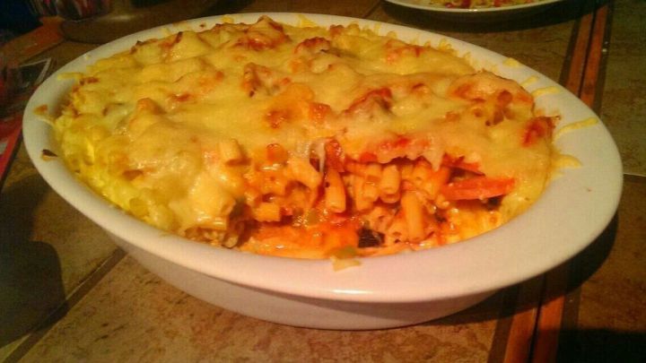 Ein Nudelauflauf mit Lyoner wird in einer wei&szlig;en Auflaufform serviert, &uuml;berbacken mit geschmolzenem K&auml;se.