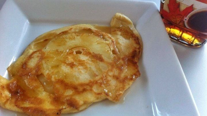 Goldene Ananas-Pfannkuchen liegen auf einem wei&szlig;en Teller, daneben steht eine Flasche mit Sirup zum Servieren.