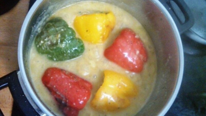 Bunte Paprikaschoten schwimmen in einer cremigen So&szlig;e, w&auml;hrend sie in einem Topf langsam garen.