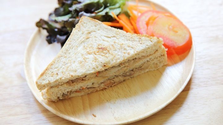 Ein Thunfisch-Brotaufstrich-Sandwich liegt auf einem Holzbrett, umringt von frischem Salat und Tomatenscheiben.