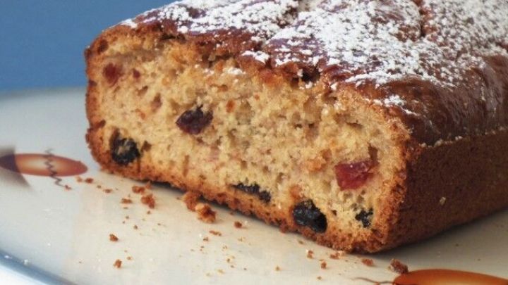 Kuchenbrot mit Fr&uuml;chten liegt auf einem Teller, mit Puderzucker best&auml;ubt und zeigt saftige Fruchtst&uuml;cke im Inneren.