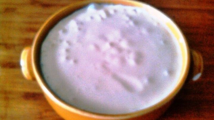 Eine gelbe Sch&uuml;ssel mit cremiger Mayonnaise steht auf einem Holztisch, umgeben von einer rustikalen K&uuml;chenatmosph&auml;re.