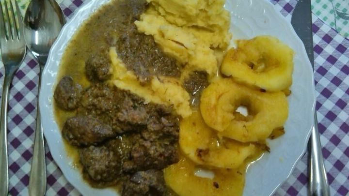 Ein Teller zeigt Putenleberragout, umgeben von p&uuml;riertem Kartoffeln und anger&ouml;steten Apfelscheiben, serviert auf kariertem Tischtuch.