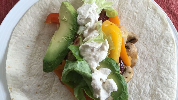 Ein Wrap mit marinierten Champignons, gef&uuml;llt mit Salat, Avocado und einer Sauce, liegt auf einem Teller.