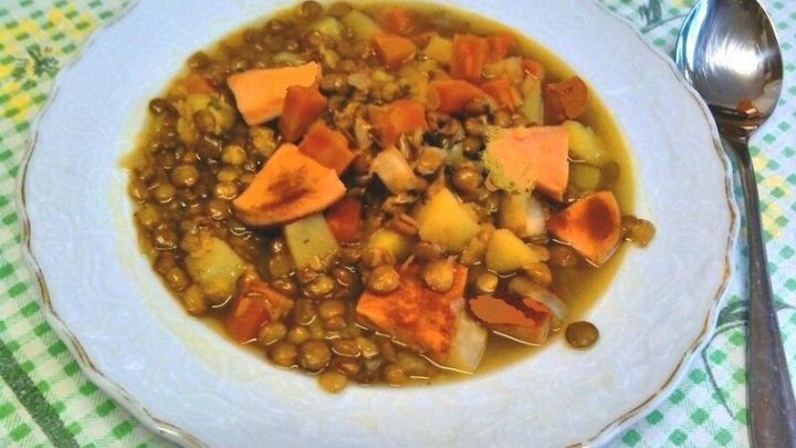 Eine Sch&uuml;ssel Linsensuppe mit Schinkenfleischwurst ist auf einem bunten, karierten Tisch gelegt, mit einem L&ouml;ffel daneben.
