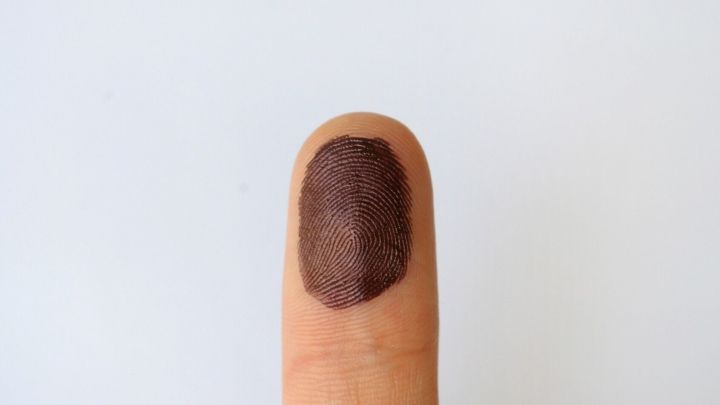 Ein Finger mit brauner Tintenkugel steht im Fokus, w&auml;hrend er auf einem wei&szlig;en Untergrund positioniert ist.