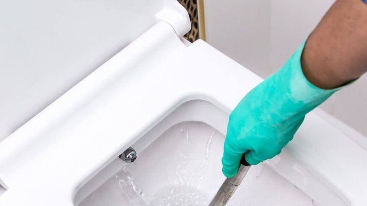 Ein gr&uuml;ner Handschuh h&auml;lt einen P&ouml;mpel, der im WC f&uuml;r die Kalkentfernung verwendet wird, in einem modernen Badezimmer.