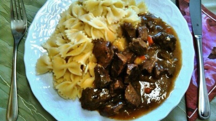 Ein Teller mit Saftgulasch neben Nudeln zeigt ein herzhaftes Gericht auf einem gedeckten Tisch.