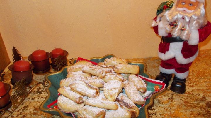 Auf einem Teller liegen gef&uuml;llte Muschelpl&auml;tzchen, umgeben von festlichen Kerzen und einer Weihnachtsmannfigur im Hintergrund.