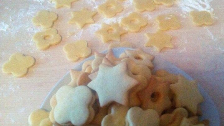 Kekse liegen auf einer bemehlten Fläche, während fertige Plätzchenteigstücke auf einem Teller zum Backen bereit sind.