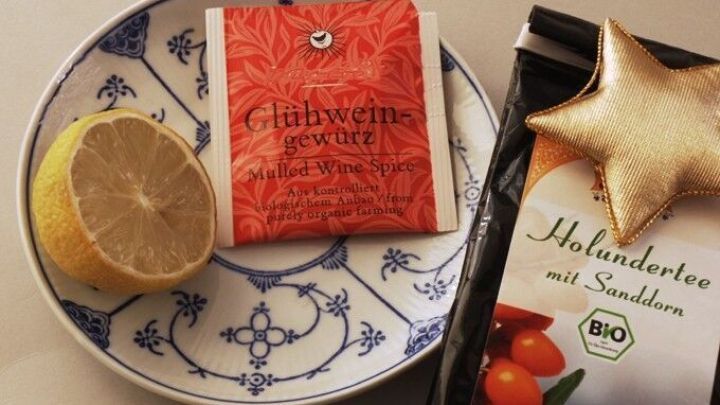 Eine Zitrone und ein Teebeutel liegen auf einem dekorativen Teller neben einer Verpackung f&uuml;r Holundertee im gem&uuml;tlichen Ambiente.