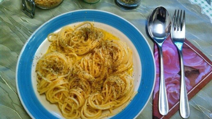 Spaghetti auf einem Teller mit Oliven&ouml;l und Knoblauchso&szlig;e, umgeben von Gew&uuml;rzen und Besteck auf einem gedeckten Tisch.