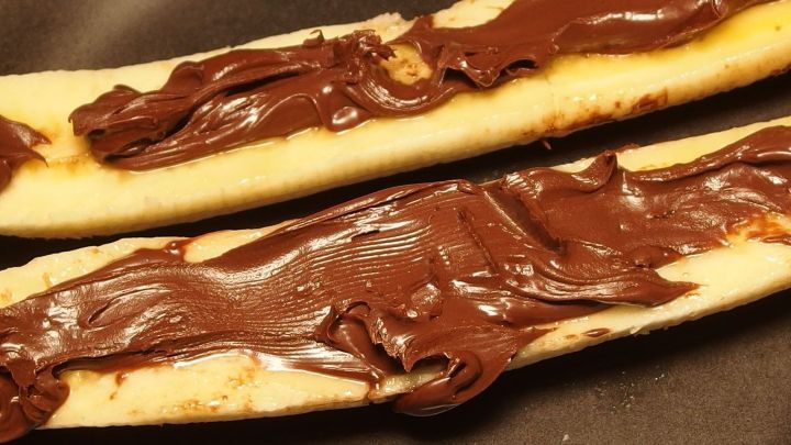 Warme Schoko-Banane liegt auf einem Teller, w&auml;hrend cremige Schokolade gleichm&auml;&szlig;ig darauf verteilt ist.