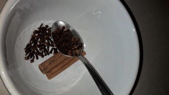 Zimtstangen und Nelken liegen in einer Sch&uuml;ssel, w&auml;hrend ein L&ouml;ffel die Gew&uuml;rze zum Mischen vorbereitet.