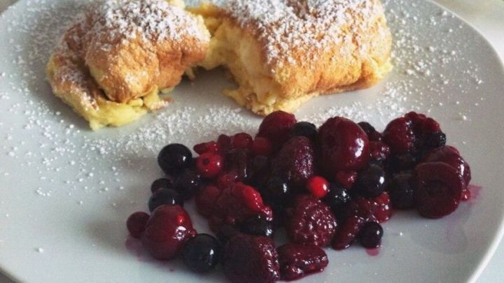 Zwei fluffige Salzburger Nockerl mit Puderzucker liegen auf einem Teller, begleitet von frischen Beeren.