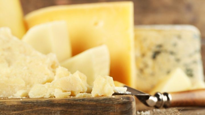 Auf einem Holztisch liegen verschiedene K&auml;sesorten und K&auml;sereste, w&auml;hrend ein Messer bereitsteht, um zu schneiden.