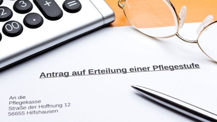 Ein Antrag auf Erteilung einer Pflegestufe liegt auf einem Tisch. Neben dem Antrag befinden sich ein Taschenrechner und eine Brille.