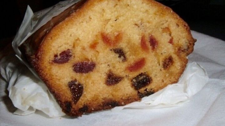Der fruchtige Kuchen mit Marzipan liegt auf einem wei&szlig;en Teller, umgeben von Backpapier, und zeigt bunte Fr&uuml;chte in der Teigmischung.