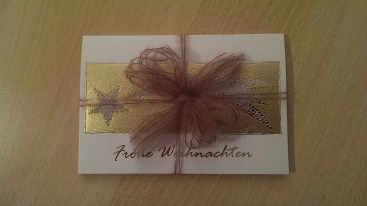 Eine mit Wolle verschlossene Weihnachtskarte liegt auf einem Tisch und ist mit einer braunen Schleife verziert.