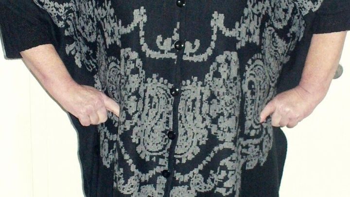 Ein schwarzer Poncho mit grauem Muster wird von einer Person getragen, die sich in einem Innenraum befindet.