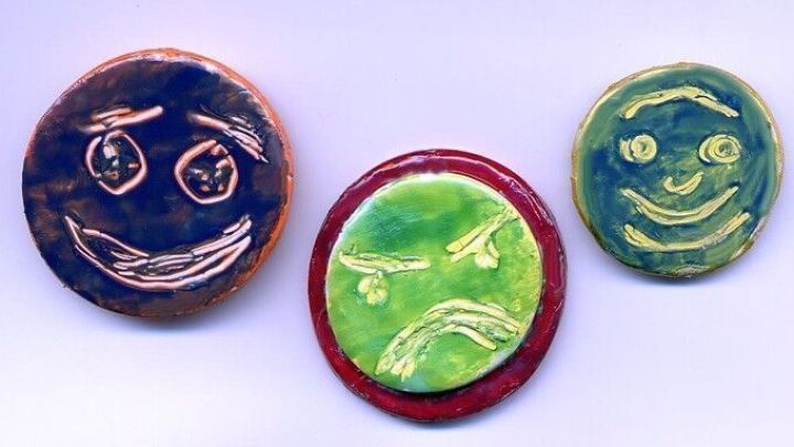 Bunte Magnetpins aus Modelliermasse mit Gesichtern zeigen eine kreative Bastelaktion vor einem hellen Hintergrund.