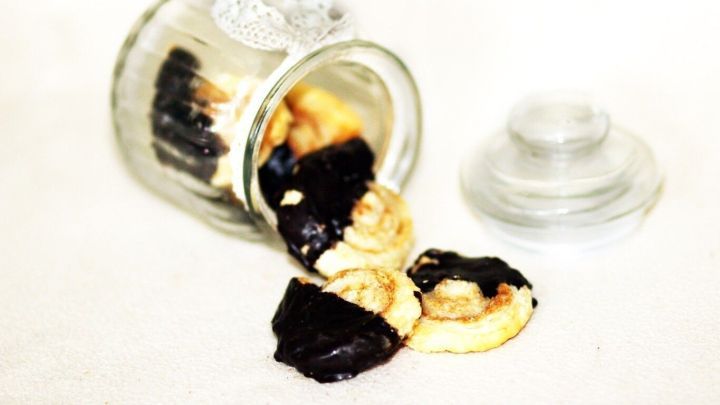 Schoko-Bl&auml;tterteig-Schnecken sind aus einem Glas gefallen, verteilt auf einer hellen Unterlage, umgeben von einem klaren Deckel.