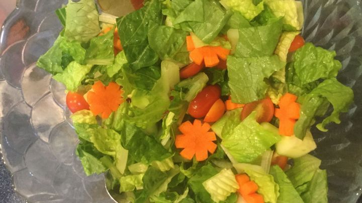 Frischer Salat enth&auml;lt gr&uuml;ne Bl&auml;tter, geschnittene M&ouml;hrenblumen und Tomaten, angerichtet in einer klaren Sch&uuml;ssel.