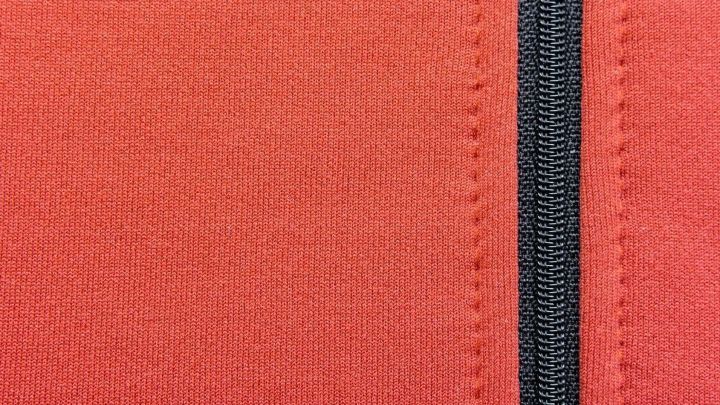 Rei&szlig;verschluss in rotem Softshellstoff, Nahaufnahme, keine sichtbaren Textinformationen.