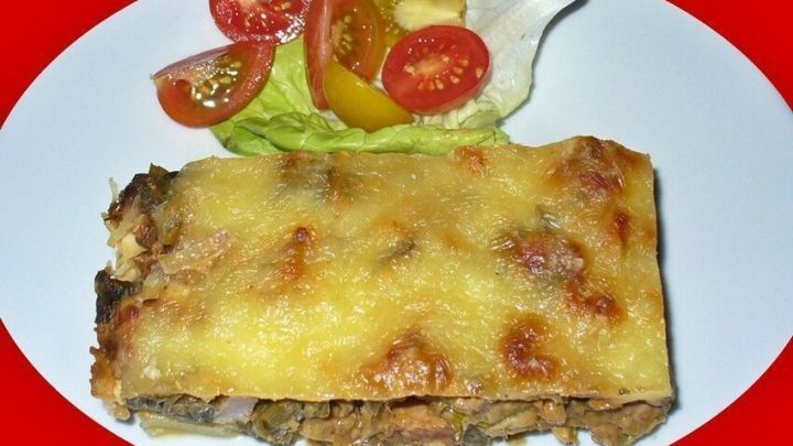 Ein goldbrauner Kartoffel-Porree-Kasslerlachs-Auflauf liegt auf einem Teller, begleitet von buntem Salad.