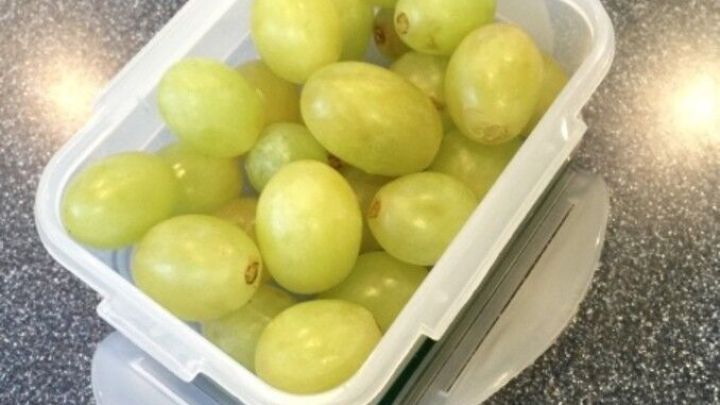 Gr&uuml;ne Trauben sind in einem transparenten Beh&auml;lter platziert und gl&auml;nzen auf einer glatten Arbeitsfl&auml;che.