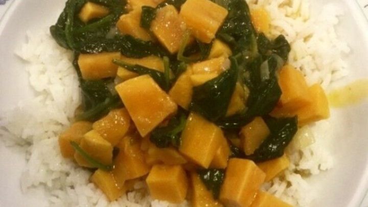 Ein bunter Teller zeigt ein vegetarisches Thai Curry aus S&uuml;&szlig;kartoffeln und Spinat auf einer Schale Reis, angerichtet auf einem blumigen Teller.