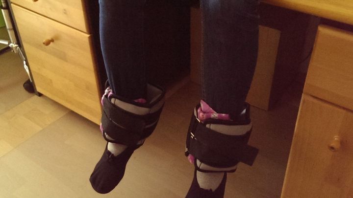 Beine h&auml;ngen entspannt von einem Tisch, Gewichtsg&uuml;rtel um die Kn&ouml;chel erleichtert die Kniebelastung.