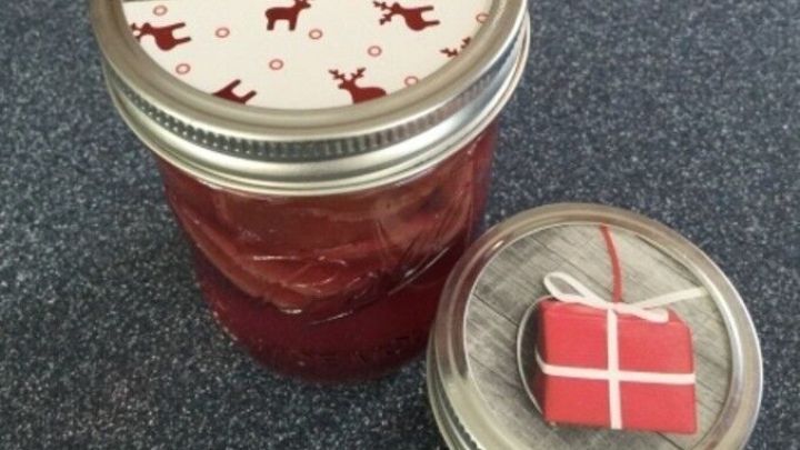 Ein Einmachglas mit roter Marmelade steht auf einem Tisch, dekoriert mit einer festlichen Weihnachtskarten-&Uuml;bertopf.