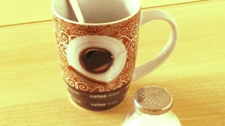 Ein Kaffeebecher steht auf einem Tisch, mit einem L&ouml;ffel darin; daneben befindet sich ein Zuckergef&auml;&szlig;. R&auml;nder an Kaffeebecher entfernen.
