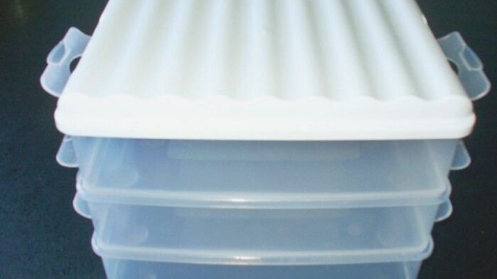 Eine transparente Aufschnittbox mit einem gerippten Deckel liegt auf gestapelten Boxen und bewahrt Wurst frisch auf.