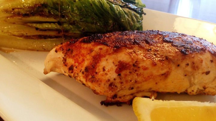 Saftiges H&uuml;hnchen liegt neben gebratenem Romanasalat auf einem wei&szlig;en Teller, garniert mit Zitronenscheibe.